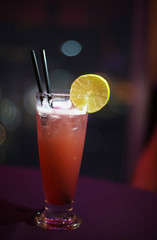 A delicious red cocktail with a piece of lemon with blurred bokeh background and two straws. Restaurant menu design. Summer refreshing drink. 