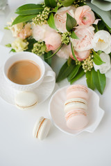 Elegant sweet dessert macarons, cup of coffee and pastel colored beige flowers bouquet