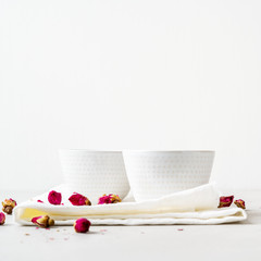 Two white cups of herbal tea with dried pink flower roses buds on gray background with copy space. Brewing and Drinking tea.