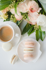 Elegant sweet dessert macarons, cup of coffee and pastel colored beige flowers bouquet
