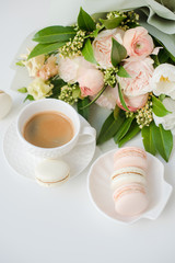 Elegant sweet dessert macarons, cup of coffee and pastel colored beige flowers bouquet