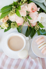 Elegant sweet dessert macarons, cup of coffee and pastel colored beige flowers bouquet