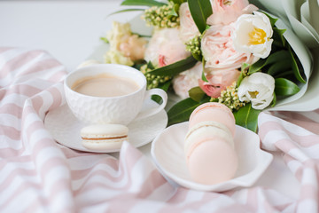 Elegant sweet dessert macarons, cup of coffee and pastel colored beige flowers bouquet