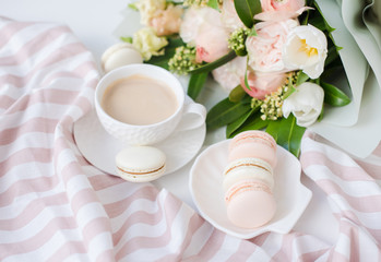 Elegant sweet dessert macarons, cup of coffee and pastel colored beige flowers bouquet