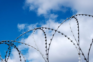 Barbed wire fence with blue sky and white clouds.