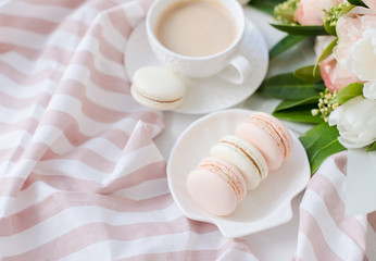 Elegant sweet dessert macarons, cup of coffee and pastel colored beige flowers bouquet