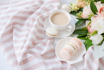 Elegant sweet dessert macarons, cup of coffee and pastel colored beige flowers bouquet