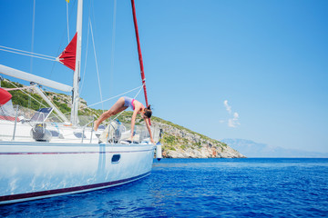 Girl jump in sea of sailing yacht on summer cruise. Travel adventure, yachting with child on vacation.