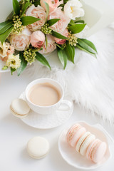 Elegant sweet dessert macarons, cup of coffee and pastel colored beige flowers bouquet