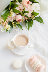 Elegant sweet dessert macarons, cup of coffee and pastel colored beige flowers bouquet
