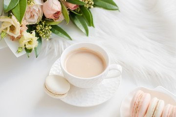 Elegant sweet dessert macarons, cup of coffee and pastel colored beige flowers bouquet