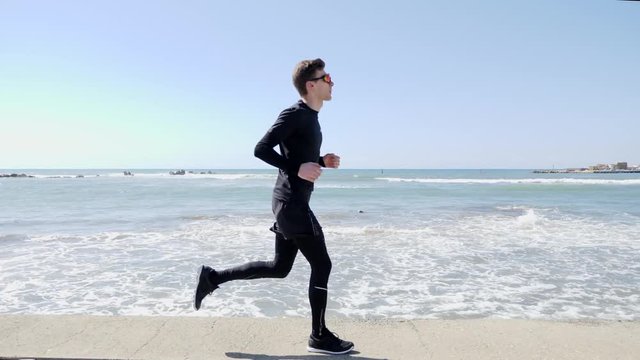 Young Attractive fit caucasian man in black joggin on a quay. Slow Motion