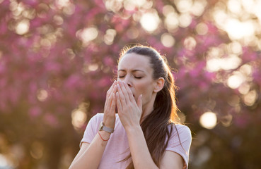 Woman sneezing because of spring pollen allergy - obrazy, fototapety, plakaty