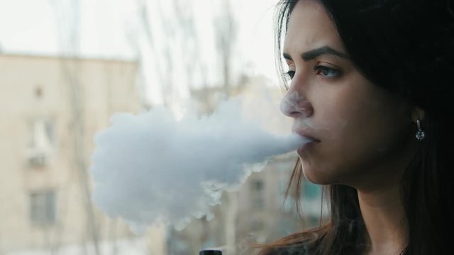 Cute pensive caucasian woman vaping outdoors. Close up