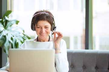 Aged woman in headset and laptop at table