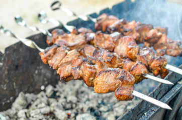 Grilled kebab frying on metal skewers. Roasted meat cooked at barbecue with smoke. Close up