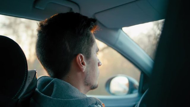 Back View Medium Close Up Shot of Young Casual Caucasian Tired Man Driving his Car at Sunset. 4K Slow Motion Stock Video