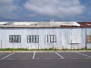 an old abandoned white industrial building with rusting patched repaired corrugated roof and boarded up windows