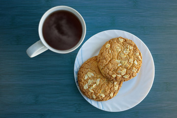 Cup of tea and saucer with two cookies with nuts on the blue table. Top view.