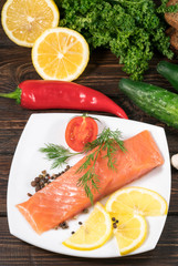 Fresh salmon fish with lemon and salad leaves on wooden table