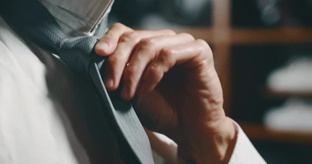 Slow motion close up of handsome businesman trying a new high quality tailor made suit and first ties a tie in atelier. - Powered by Adobe