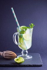 Mojito cocktail on black background. Mojito with lime and fresh mint on slate board. Summer refreshing cocktail and wooden juicer on dark background. Infused water