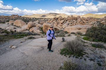 Fototapeta premium Young woman female hiker wearing a backpack starts off on a hiking trail in Joshua Tree National Park, to the Arch Rock