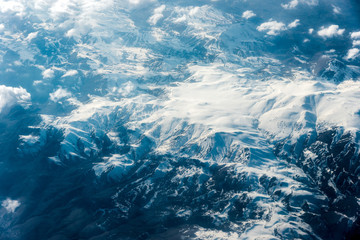 Top view of white clouds between which you can see high mountains