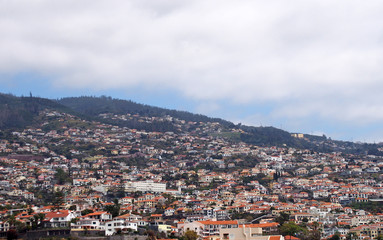 Fototapeta na wymiar a wide panoramic view of the city of funchal in madeira with houses and tree covered hills under a cloudy sky