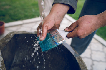 Close up on hands of a craftsman washing a brush cleaning after the painting work finished job