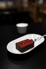 Brownie with with vivid red dry raspberry spices with a cup of cappuccino coffee in the background