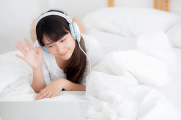 Beautiful young asia woman lying in bedroom using laptop computer showing video call chat at home, girl greet and listen and talking messenger, communication and lifestyle concept.