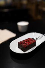 Brownie with with vivid red dry raspberry spices with a cup of cappuccino coffee in the background