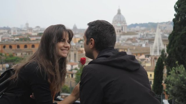 Romantic couple kissing, man give a flower to woman, Rome, European city panorama in background