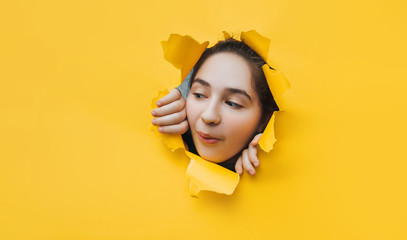 Funny teenage girl peeping through hole on yellow paper. The concept of surprise, joyful mood from...