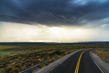 Highway road against the background of rain dark clouds, steppes, and mountains in Patagonia, Argentina