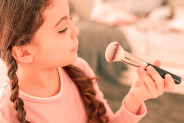 Nice pleasant girl looking at the makeup brush