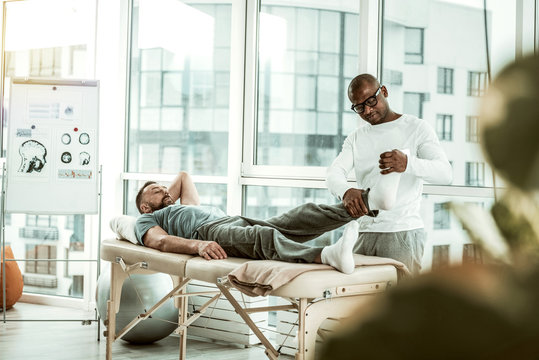 Serious dark-skinned therapist checking foot of his patient
