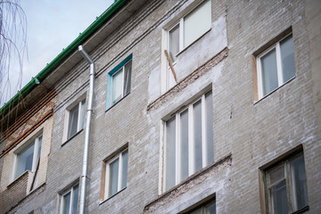 Fototapeta premium Broken concrete balcony on the facade of the building. Restoration of an old residential gray plastered house. White plastic windows and an exit with a door.