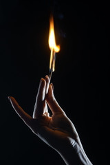 elegant female hand holding burning match on dark background  
