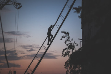 A man descends a metal staircase in the dark at sunset.