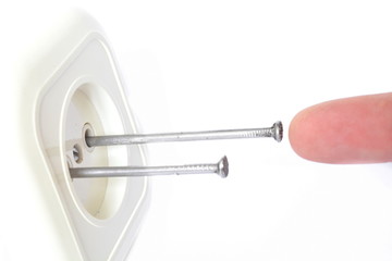 Concept accident prevention - finger touches to shove metal nails in the hole of electrical outlet on white background. Isolated