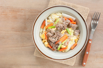 top view of stir fried glass noodle with pork and vegetable in a ceramic dish on wooden table. asian homemade style food concept.