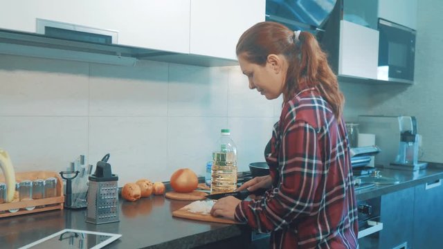 woman mom cooking in the kitchen concept. cooks soup in a pan and cutting onions on a wooden board. girl mother in the kitchen indoors preparing food lifestyle concept smart home control on a digital