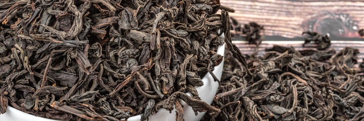 Dried tea is poured into a ceramic cup on a wooden plank table.