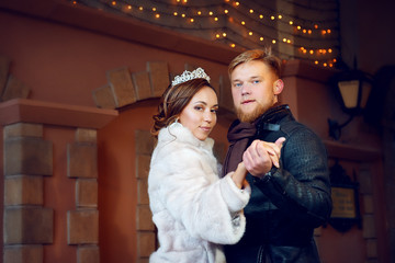 Portrait of the bride and groom in a dance position on a winter day against the background of a vintage wall with flashing garlands.