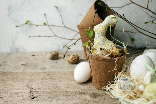 Happy Easter concept - Easter eggs and bunny rabbit in flower craft potty and fresh greenery branches on dark rustic wooden background, copy space