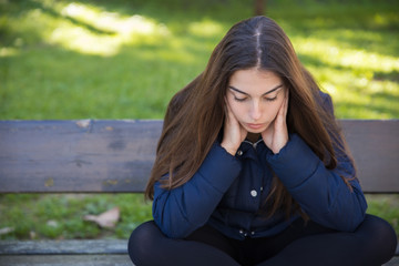 Pensive pretty woman sitting on bench in park