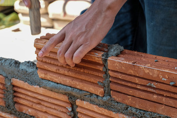 Bricklayer worker installing brick masonry on exterior wall.