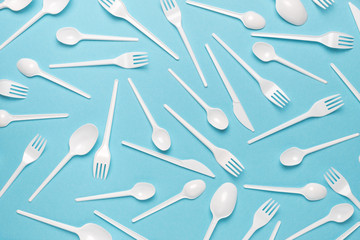 Plastic disposable forks and spoons on a blue background. Abstract background of plastic utensils.